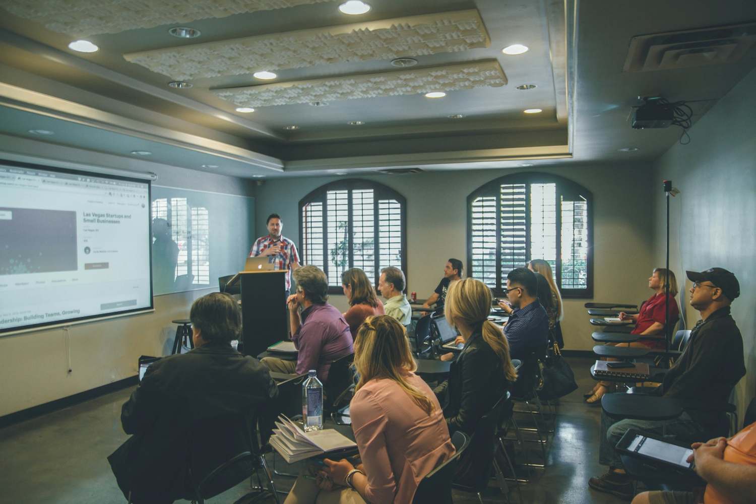 Relatore davanti a una platea in una sala di formazione, con schermo di proiezione